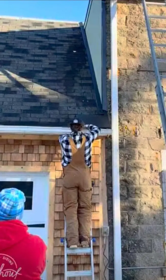 Roofer on a ladder working at the roof edge of a house